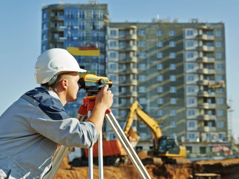 Surveyor checking boundary measurements on an urban infill site near existing buildings before layout and design planning.