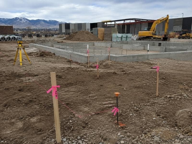 Construction Staking markers beside an unfinished building foundation during a delayed project restart in Denver, Colorado.